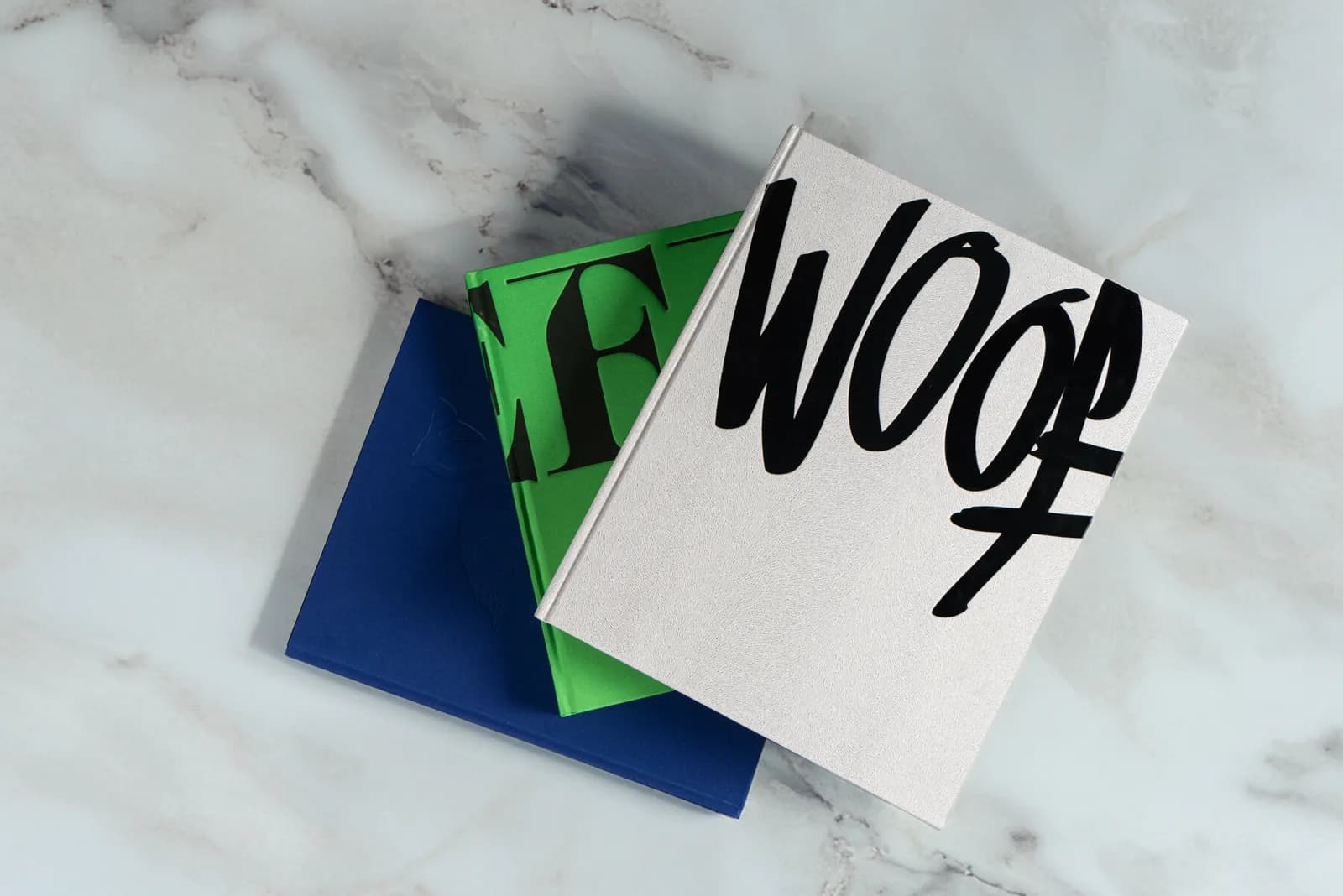 WOOF apilado con otros libros de la editorial sobre mármol