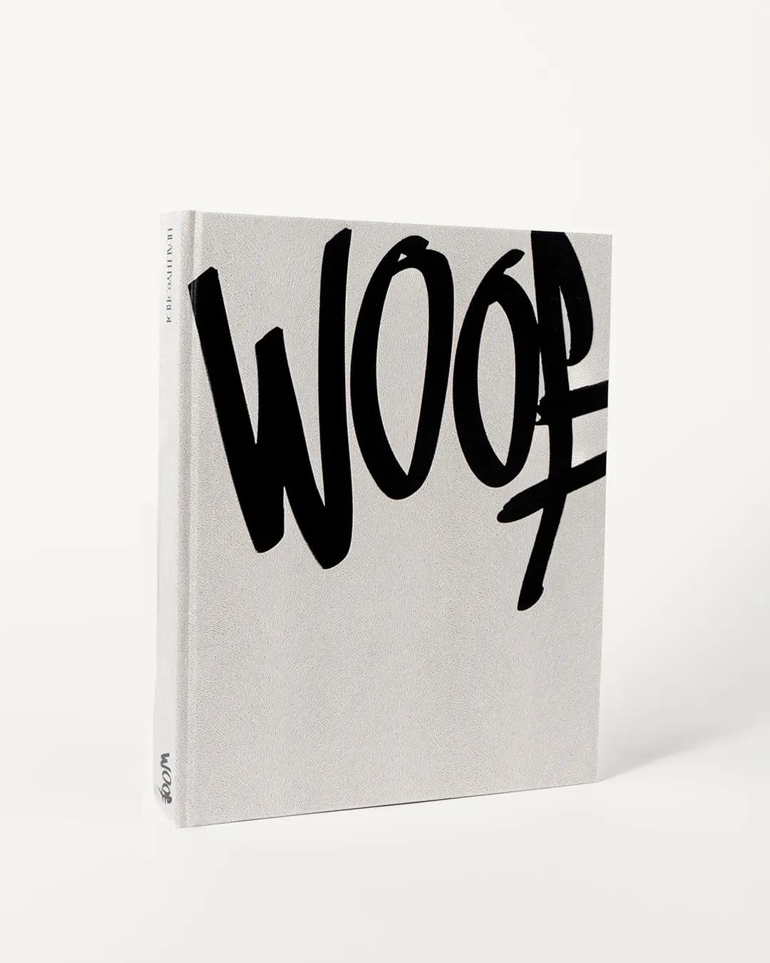 El libro WOOF de pie, portada blanca con el trazo negro del logo